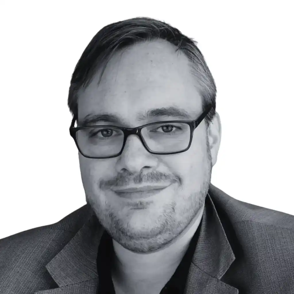 A person with short hair and glasses, wearing a suit jacket and a slight smile, is shown against a plain white background, representing their expertise in digital marketing agency work. Opdee Digital Marketing