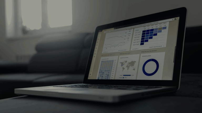 A laptop on a dark couch displays data dashboards with charts, maps, and graphs—ideal for analyzing and scaling social media strategy. The room is dimly lit, with a window in the background adding to the focused workspace atmosphere. Opdee Digital Marketing
