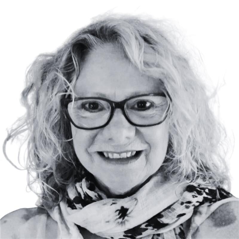 A woman with curly light hair, wearing glasses and a patterned scarf, smiles at the camera against a plain white background—an inviting introduction to our About Us page. Opdee Digital Marketing